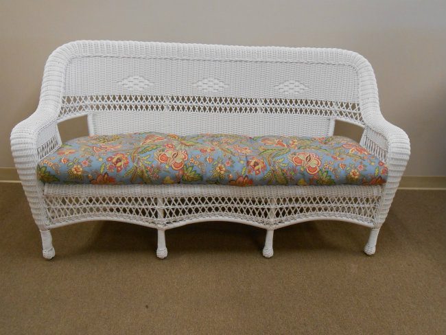 An image of white wicker furniture with a pink and blue printed seat cushion.