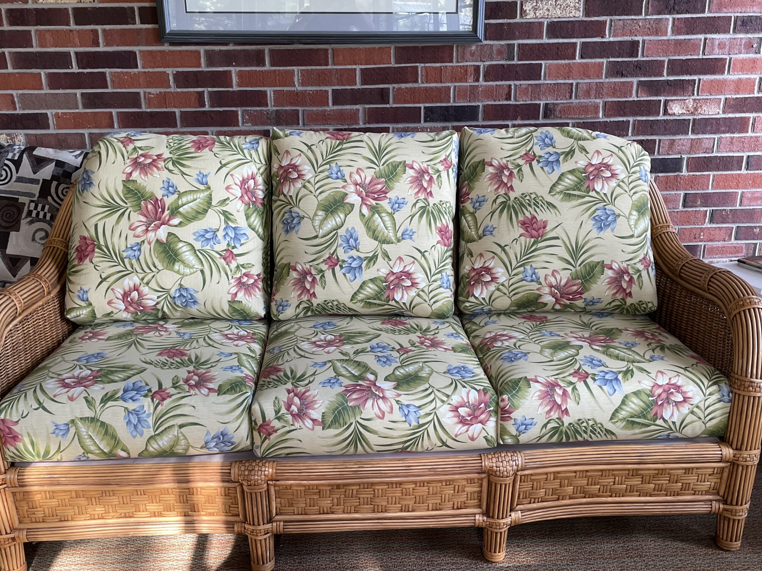 An image of floral cushions on a brown wicker outdoor loveseat.