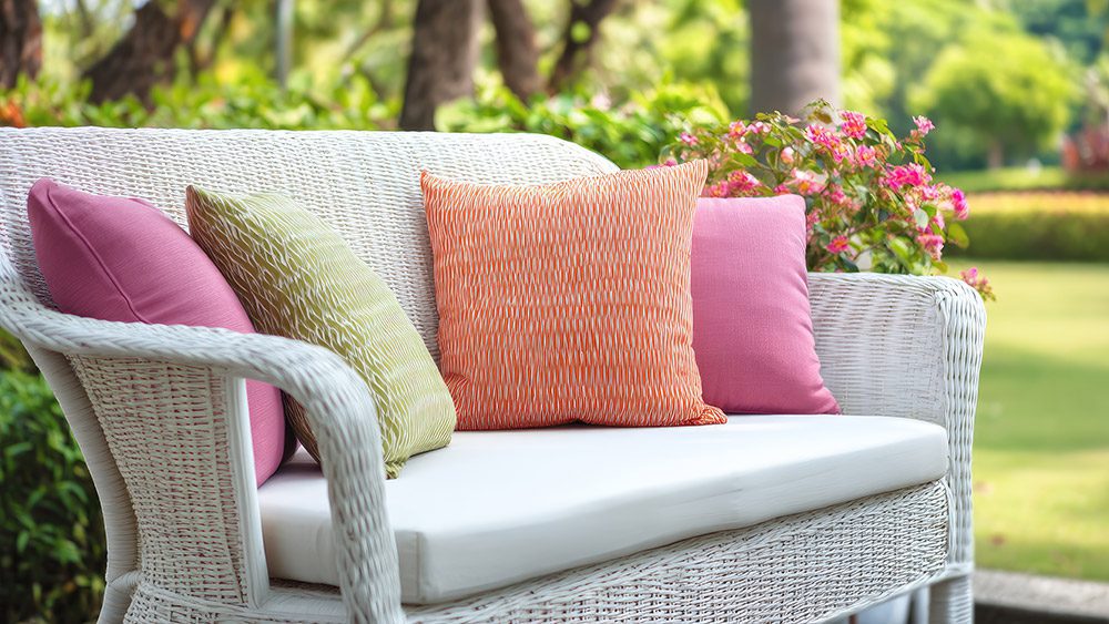 A white, wicker loveseat sitting in the sun.